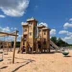 Estructura de madera del parque infantil con torres y toboganes bajo cielo azul