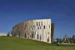 Ángulo lateral del edificio mostrando su diseño curvo y revestimiento de madera sobre colina verde