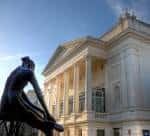Fachada principal del Royal Opera House con estatua en primer plano bajo luz diurna