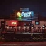 Fachada nocturna del Lonesome Rose con letrero iluminado y escenario al aire libre