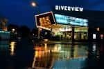 Fachada exterior del Riverview Theater de noche con letrero iluminado