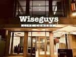 Fachada exterior nocturna del Wiseguys Comedy Club con letrero iluminado