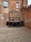 Escenario histórico al aire libre dentro del museo, mostrando una estructura de madera sobre patio empedrado
