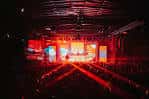 Escenario iluminado en rojo con estructura de techo industrial y asientos dispuestos