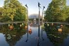 Escultura moderna junto al estanque con reflejos y árboles frondosos