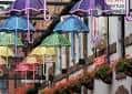 Decoración festiva con sombrillas de colores colgando sobre una calle peatonal, ideal para eventos al aire libre o celebraciones temáticas