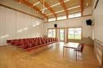 Interior de la sala principal con asientos rojos dispuestos en filas y techo de vigas de madera