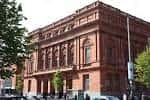 Ángulo lateral de la Biblioteca Central de Belfast con árboles y vehículos en primer plano