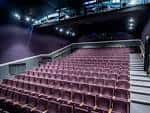 Interior del auditorio con butacas rojas y escenario iluminado