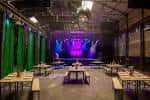 Interior del espacio de eventos con escenario iluminado en tonos morados y mesas dispuestas para una recepción