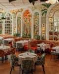 Interior del salón principal con mesas redondas, sillas tapizadas y decoración mural colorida
