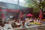 Terraza exterior del Hyde Park Book Club con mesas y sombrillas rojas