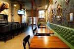 Interior del pub con mesas de madera y bancos tapizados en verde