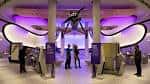 Interior del museo con exhibición de dinosaurio suspendido y visitantes explorando la sala