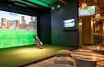 Zona de simulación de golf indoor con pantalla grande y ambiente relajado