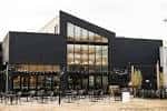 Fachada moderna del Other Half Brewing Company con grandes ventanales y zona de asientos exteriores