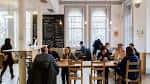 Interior del centro con personas reunidas en mesas, ambiente acogedor y luminoso