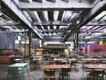 Interior del espacio de eventos con mesas y sillas dispuestas bajo estructura industrial