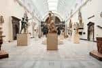 Galería interior del museo con esculturas en pedestales y techo de cristal