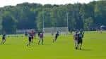 Jugadores practicando fútbol sobre césped verde con vallas y bosque al fondo