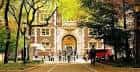Entrada principal del campus con arco central y personas caminando entre árboles en otoño