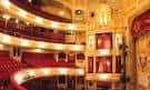 Interior del auditorio con balcones curvos, butacas rojas y decoración dorada elegante