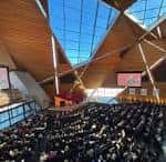 Auditorio lleno durante un evento con pantallas laterales y techo acristalado