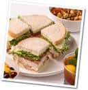 Plato de sándwiches cortados en cuartos con ensalada y bebida en mesa