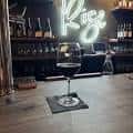 Detalle de copa de vino en el mostrador con neón 'Rise' al fondo
