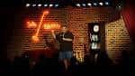 Comediante en el escenario con el logo de Side Splitters iluminado