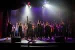 Escenario con grupo de personas en actuación bajo luces de teatro