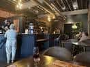 Interior del bar con clientes sentados en mesas y barra de servicio