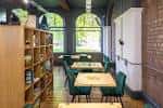 Zona interior del café con sillas verdes y ventanas arqueadas