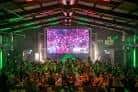 Escenario iluminado con luces de colores y multitud en el interior del The Nest para una fiesta o concierto