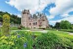 Vista frontal del castillo con jardines floridos y cielo azul