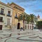 Vista panorámica de la Plaça de Baix con edificios históricos y palmeras bajo un cielo azul