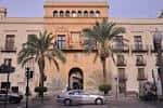 Fachada principal del Ayuntamiento de Elche en la Plaça de Baix, con banderas y palmeras a los lados