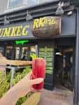 Entrada del establecimiento con letrero de 'RumKeg876' y bebida en primer plano