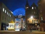 Fachada nocturna de Victoria Square iluminada, destacando la cúpula brillante y el entorno urbano