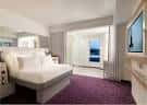 Habitación premium con cama king-size, alfombra morada y vista a la ciudad desde el balcón
