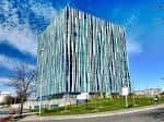 Fachada frontal de la Biblioteca Sir Duncan Rice bajo un cielo azul con nubes dispersas