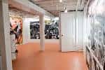 Interior de la galería artística HAIR + NAILS con obras expuestas y suelo naranja
