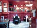 Interior acogedor de Milo Lounge con paredes rojas, mesas y decoración artística en las paredes