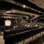 Interior del auditorio con butacas negras y escenario iluminado