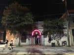 Entrada principal del bar por la noche con arco luminoso rosa y ambiente urbano