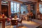 Zona íntima del venue con mobiliario acogedor, estanterías decorativas y grandes ventanales que permiten luz natural