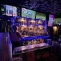 Interior del bar con estantería de botellas iluminada y pantallas