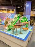 Interior del museo mostrando una zona interactiva para niños con tobogán verde y elementos educativos