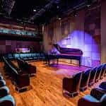Interior del auditorio con piano en el escenario y butacas azules