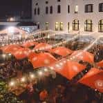 El Biergarten de Urban Chestnut iluminado por la noche con luces festivas y mesas ocupadas